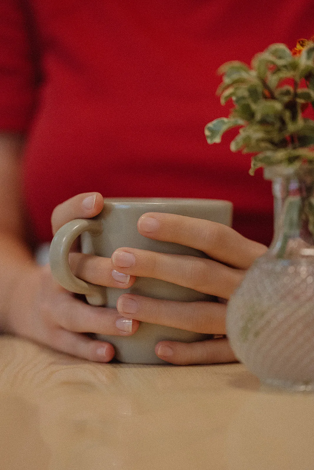 Les mains de Vinciane autour d'une tasse de thé, à côté d'un petit bouquet